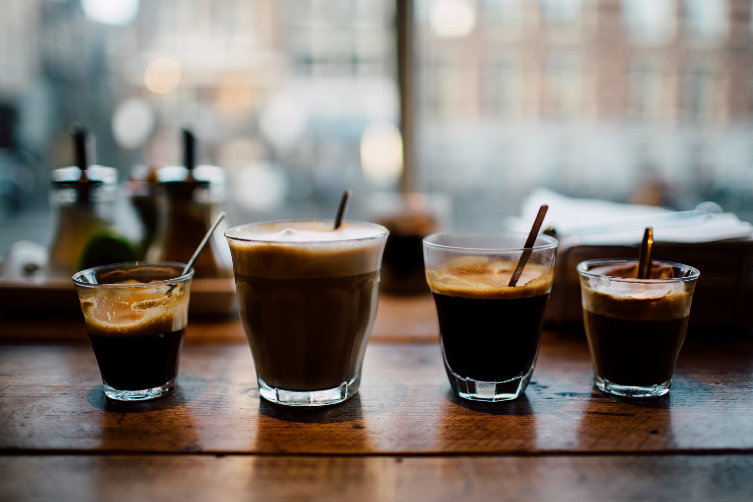 Selection of espresso and latte coffee served in glasses on wooden café table. Taste the variety of brews today.